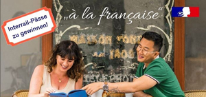 2 Studierende sitzen im Außenbereich eines französischen Cafés, mit dem Logo der französischen Botschaft sowie dem Sticker "Interrail-Pässe zu gewinnen!"